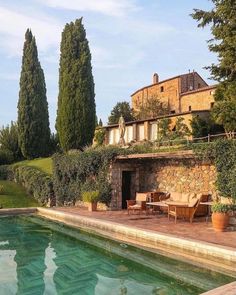 an outdoor swimming pool in front of a stone building with trees and bushes around it