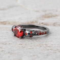 a close up of a ring with a red stone in the middle and two skulls on it