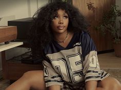 a woman sitting on the floor with her legs crossed and wearing a football jersey shirt