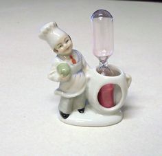 a small white figurine with a chef holding a green object in it's hand