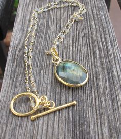 "A mesmerizing gold plated over sterling silver necklace featuring an oval-shaped faceted Labradorite that has mesmerizing hues of green and gold, suspended from a hand wire wrapped labradorite beaded 16\" chain fastened with a gold plated silver brushed toggle clasp.(n-150) Labradorite measure 20mm x 16mm 16\" Chain Length Makes the perfect bridesmaids necklace as there are 7 pieces available. *LIKE* us on Facebook http://www.facebook.com/Belesas to find special coupon codes, *FOLLOW* us on Twi Gold Labradorite Necklace With Gemstone Beads, Gold Oval Labradorite Necklaces, Gold Oval Pendant Necklace In Labradorite, Gold Labradorite Oval Pendant Necklace, Gold Oval Labradorite Necklace, Oval Gold Labradorite Necklace, Gold Necklaces With Natural Labradorite Stones, Gold Labradorite Necklaces With Natural Stones, Oval Labradorite Necklace For Jewelry Making