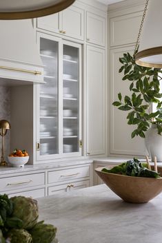 a bowl of vegetables sits on the counter top in this white kitchen with gold accents