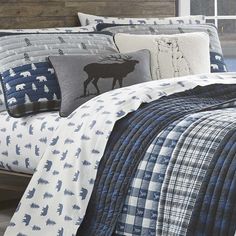 a bed covered in blue and white comforter next to a wooden headboard with a moose on it