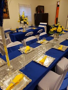 a table set up with silver and yellow napkins, place settings, and centerpieces