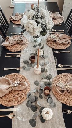 a dining room table set with place settings, napkins and flowers in vases