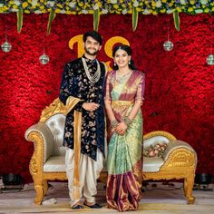 a man and woman standing next to each other in front of a red wall with flowers