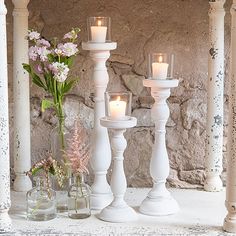 three white candles sitting on top of a table next to vases filled with flowers