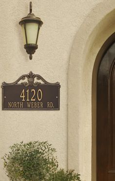 a house number sign mounted to the side of a white building with a potted plant next to it