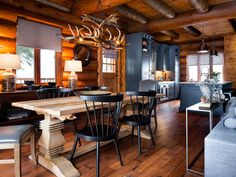 a dining room table and chairs in front of a kitchen with wooden walls, wood flooring and large windows