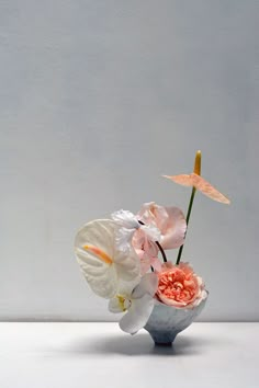 a vase filled with flowers on top of a white table next to a gray wall