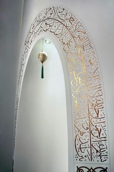 an arch with arabic writing on it and a light hanging from the ceiling in front of it