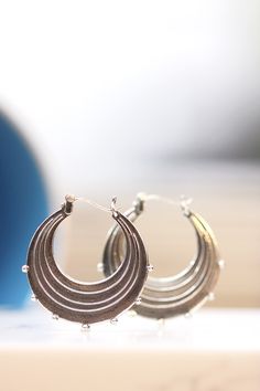 "Evocative of raindrops striking a pool of water, circles radiating outward from the point of impact and smaller droplets becoming airborne. These earrings are made completely of sterling silver, right down to the ear wires which are hinged and connect in a catch on the other side. The line and ball design is repeated on both sides of each earring. Each hoop measures approximately 1.25\" in diameter. The hoops have been given a patina to darken them and then tumbled in steel shot to give them a Unique Teardrop Hoop Earrings For Everyday, Hypoallergenic Silver Hoop Earrings In Brass, Metal Drop Hoop Earrings With Ear Wire, Nickel-free Metal Drop Hoop Earrings, Round Teardrop Earrings For Everyday, Everyday Round Teardrop Pierced Earrings, Metal Teardrop Hoop Earrings For Pierced Ears, Pierced Round Metal Wrap Earrings, Metal Round Wrap Earrings