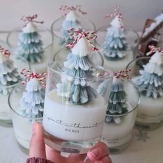 a person holding up a glass with candles in it and small christmas trees on the side