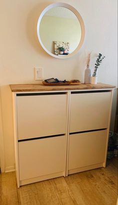 a white dresser with two drawers and a round mirror on the wall above it in a room