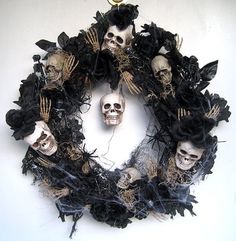 a wreath made out of fake skulls and black feathers is displayed on a white wall