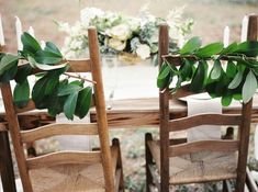 two wooden chairs sitting next to each other near a table with flowers and candles on it