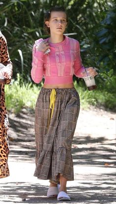 two women walking down the street while one holds a drink in her hand and another wears a pink sweater