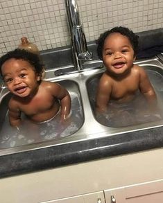 two babies are sitting in the kitchen sink