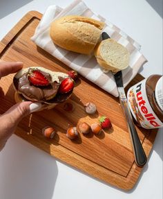 a wooden cutting board topped with a sandwich covered in chocolate frosting and strawberries