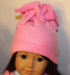 a doll is wearing a pink hat and coat with a bow on the top of it