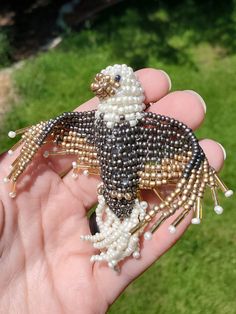 a hand holding a beaded brooch in the shape of a bird on grass