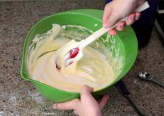 two hands mixing batter in a green bowl