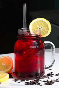 a jar filled with liquid next to sliced lemons and black tea on a table