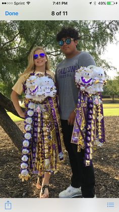 two people standing next to each other in front of a tree with purple and gold decorations