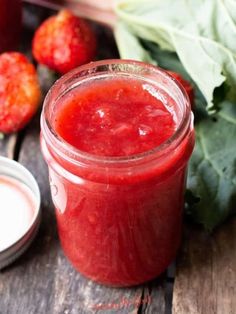 a glass jar filled with strawberry jam next to fresh strawberries and spinach leaves