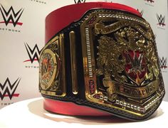 a large gold and red wrestling belt on display in front of a white wall with the wwe logo