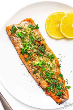 a white plate topped with a piece of salmon next to lemon wedges and a fork