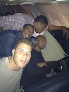 four men sitting on an airplane looking at the camera