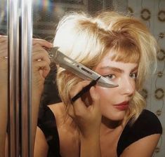 a woman holding a pair of scissors in front of her face while looking into a mirror