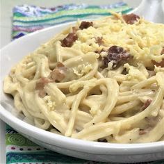 a white bowl filled with pasta and meat on top of a colorful table cloth next to a fork