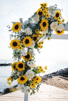 a cross decorated with sunflowers and white roses on a wooden walkway near the water