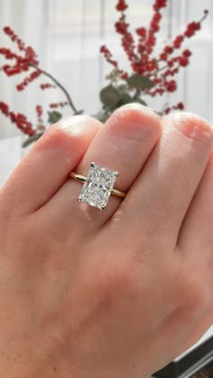 a woman's hand holding a diamond ring in front of a vase with red flowers