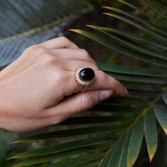 a woman's hand with a ring on it and palm leaves in the background