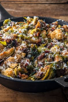 an iron skillet filled with cooked vegetables on top of a wooden table next to a spoon