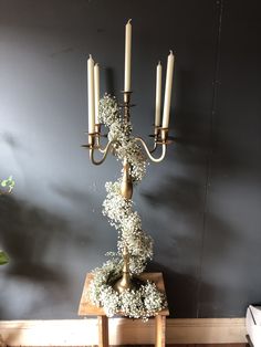 a tall candelabra with flowers and candles on it in front of a gray wall