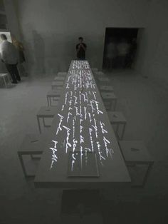 a long table with people standing around it in the middle of an empty room filled with white tables