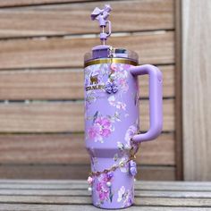 a purple coffee mug with flowers on it sitting on a wooden table next to a bench