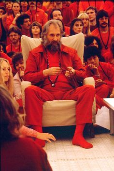 a man in red sitting on a white chair next to a group of people with long hair and beards