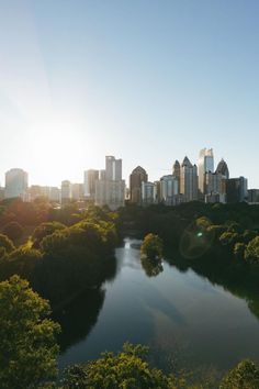 the sun shines brightly over a city skyline as it reflects in a lake surrounded by trees