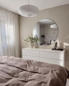 a bedroom with a bed, dresser and large round mirror on the wall above it