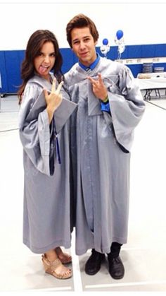 two people in graduation gowns posing for the camera