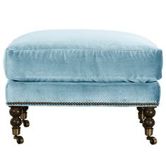 a blue ottoman with wooden legs and studding on the bottom, in front of a white background