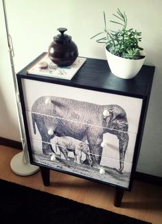 an elephant and two baby elephants on top of a night stand next to a potted plant