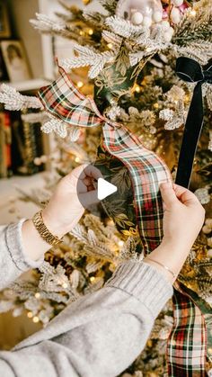 a woman is decorating a christmas tree with plaid ribbon and black bow on it