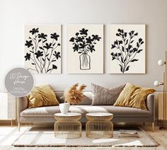 three black and white flowers in vases on the wall above a couch with pillows