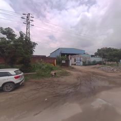 a white car parked in front of a blue building on a dirt road with power lines above it